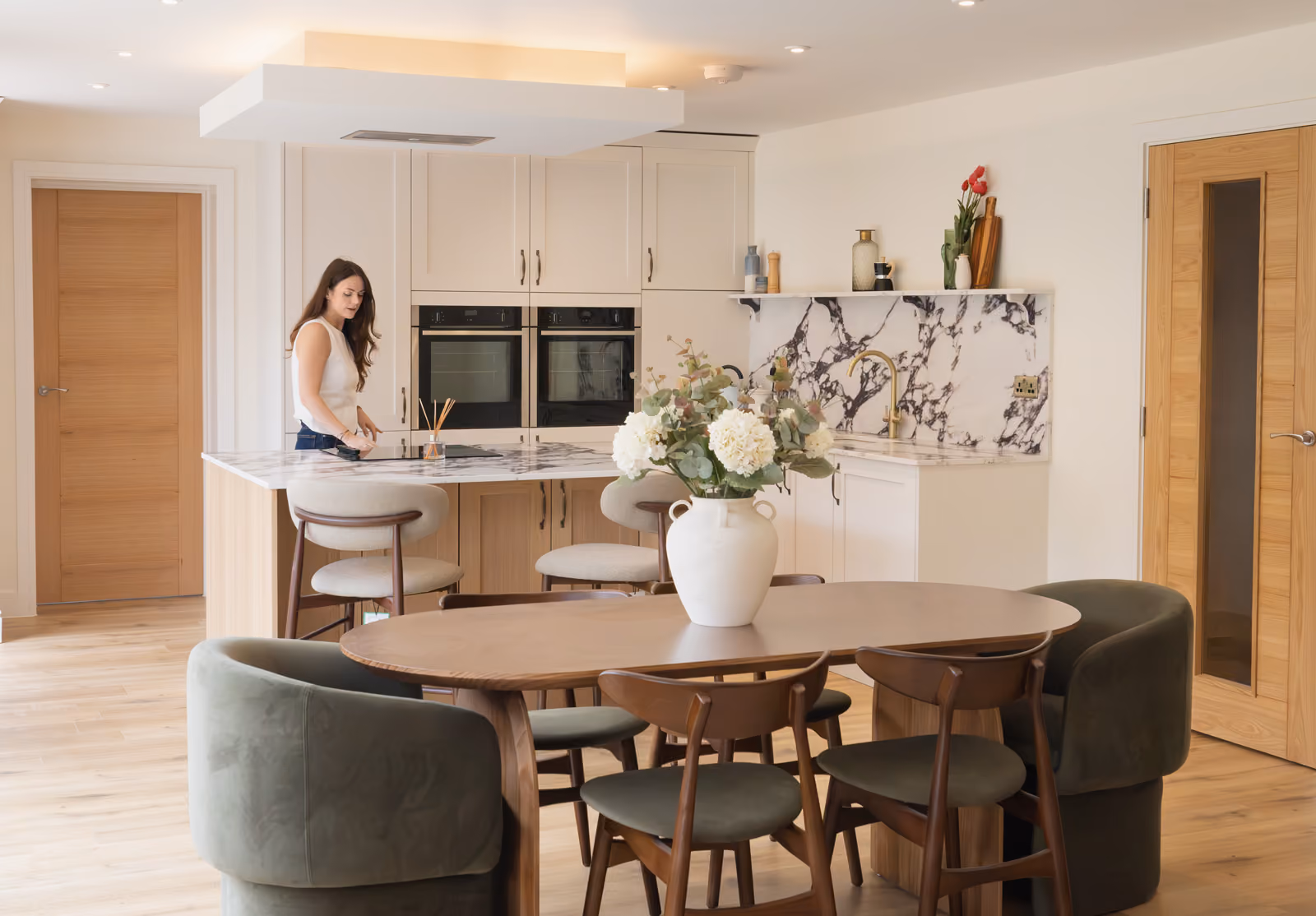 Rosey Cassidy standing in a modern kitchen with marble countertops and wooden dining table.